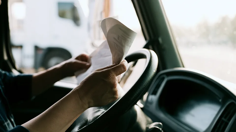 Mão de motorista segurando um documento sobre o volante do caminhão